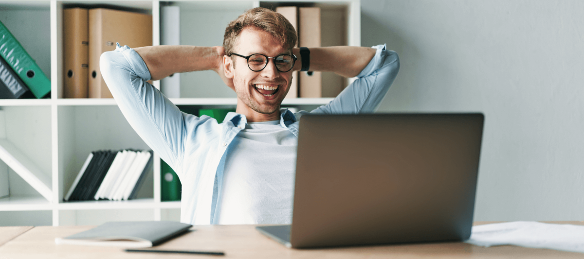 Young man smiling as he reads the screen of a laptop computer while relaxing working at a wooden table at home